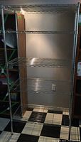 Full view of the empty 5-shelf metal wire storage rack standing upright in a room with checkered floor tiles.