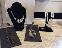 Five necklaces displayed on black necklace stands and gray pads. Includes silver-tone sparkly choker, gold-tone 3-chain with bead accents, silver-tone multi-chain with glass, wood and metal beads, and faux pearl strands.