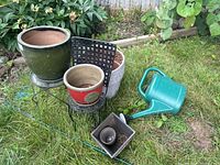Outdoor items set on grass including ceramic pots, metal plant stands, and a green watering can
