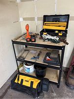 Photo of the metal tool bench with multiple tools and accessories placed on and under it including cordless drill, hand tools, extension cords, and tool kits.