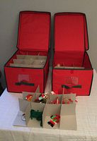 Two red cloth-sided ornament storage boxes with cardboard inserts shown open on a table, displaying the ornaments inside.