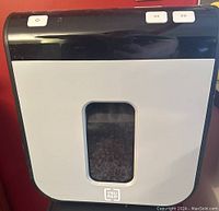 Front view of a TruRed paper shredder showing white front panel with a small window to view shredded paper inside the bin and control buttons on top edge.