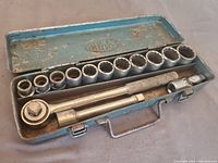 Open metal case showing organized socket set including ratchet, extension, and sockets varying from smallest to largest size.