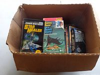 Photo of cardboard box filled with paperback science fiction books including Star Healer and Danny Dunn on a Desert Island.