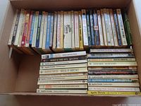 Box containing over 60 used paperback Agatha Christie books, mostly arranged vertically and some stacked horizontally. Various titles visible.