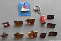 Collection of various Coca-Cola enamel pins and a keychain on gray background