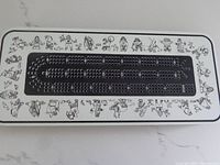 Top-down photo of the metal cribbage board with Inuit art and peg holes.