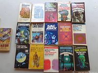 Photo showing 17 Isaac Asimov books arranged on a surface, showcasing various titles of used paperback books with colorful space and science-themed covers.