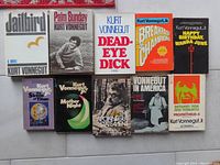 Top-down view of 10 Kurt Vonnegut books, arranged in two rows showing covers including Jailbird, Palm Sunday, Dead Eye Dick, Breakfast of Champions, Happy Birthday Wanda June, The Sirens of Titan, Mother Night, The Vonnegut Statement, Vonnegut in America, and Between Time and Timbuktu.