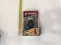 Front view of the LEGO Ninjago Black Ninja LED keychain light in original packaging next to a ruler for size reference.