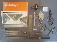 Overview of Mitutoyo and other branded machine shop tools spread on surface including combination square, rulers, dividers, bevel protractor, feeler gauges.