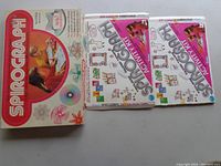 Photo showing the original Spirograph box with colorful packaging and two instruction or activity booklets placed beside it.