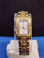 Front view of the Croton Swiss watch showing rectangular gold plated case, white dial with Roman numerals and gold hands, and gold plated multi-link bracelet.