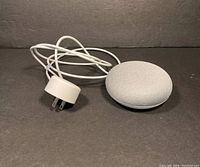 Google Home Mini smart speaker and power adapter displayed on dark surface.
