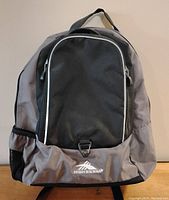 Front view of the medium sized High Sierra backpack with grey and black panels, front zipper pocket, and logo visible.