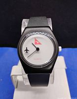 Black case quartz wristwatch with white dial featuring red Qantas logo and black airplane motifs. Watch has a black rubber strap and visible wear on the face.