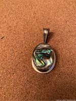 Front view of oval sterling silver pendant with abalone shell inlay on a cork surface