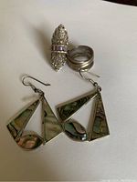 Sterling silver saddle-shaped ring with light purple stones alongside two Mexican silver Alpaca earrings with abalone shell inlays.