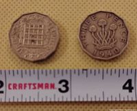 Photo showing the obverse and reverse sides of the 1940 King George VI threepence coin next to a measurement tape.
