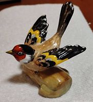 Side view of the vintage Crown Staffordshire goldfinch bird figurine showing the detailed color painting and the poised position on a wood-like base.
