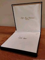 Open Fifth Avenue Collection hand made jewelry box revealing white satin interior with hooks for necklace display and cushioned base. Black exterior.