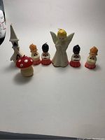 Front view of seven vintage candles including an angel, four small figures, a church, and a red mushroom