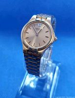 Front angle close-up of the watch showing gold-tone case and dial with simple hour markers and black hour and minute hands.