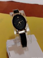 Front view of the women's dress watch showing the black oval dial with gold-tone hands and four small rhinestone markers, gold-tone case, and part of the bracelet-style band with black and gold-tone elements.