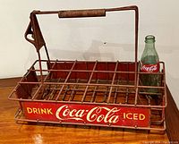 Front and left-side view of red metal wire Coca-Cola carrier with one modern Coke bottle inserted