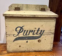 Front view of a rectangular wooden box painted yellow with black 'Purity' logo on the front side.