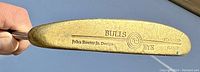 Close view of putter blade stamped with Bulls Eye and John Roster Jr. Design, showing brass/bronze toned metal with patina and wear.