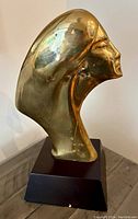 Front right quarter view of brass head sculpture on wooden base showing overall form