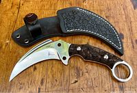 Full view of karambit knife alongside skull-embossed leather sheath on wooden background.