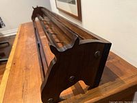 Close-up photo of the dark wooden coat rack showing carved horse head detail on one end, hooked hanging section visible
