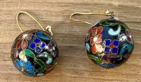 Close-up of pair of round cloisonné enamel ball earrings showing floral design and gold-tone hooks