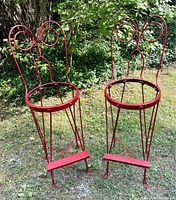 Pair of vintage red cast iron twist bar stools in outdoor setting, showing overall condition and design.