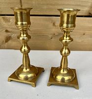 Pair of solid brass vintage candlesticks side by side on white surface with wood background