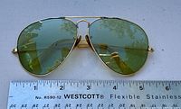 Front view of vintage Ray Ban aviator sunglasses with green lenses and gold frame, positioned above a ruler showing approximately 5 inch lens width.