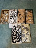 Seven trays of assorted silver-tone necklaces, bracelets, earrings, rings and pins displayed on carpet