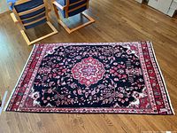 Full view of the area rug showing intricate floral and vine design on a dark navy background with red and white borders laid on wooden floor.