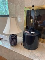 Two ceramic lamps shown on marble surface near fireplace; one with patterned base and shade, other solid base without shade.