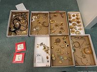 Six trays of assorted gold-tone jewelry pieces laid out on carpet