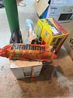 Full view of the lot showing a red-yellow Duraflame fire log with torn packaging, yellow box of charcoal, and lighter fluid bottle on top of a box.