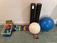 Full overview of the exercise equipment lot showing foam rollers, two exercise balls, multiple hand weights, and the container with fitness bands and other accessories.
