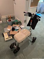 Photo of Swivelmate knee walker with white padded seat, foldable frame, and attached black storage bag along with various medical and health aids scattered nearby