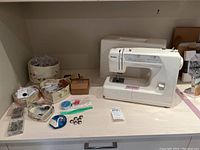 Full view of Kenmore sewing machine with assorted sewing notions displayed on white surface along with cover case in background
