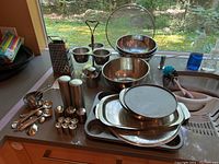 Wide overhead view of the entire set on countertop including bowls, colanders, grater, measuring cups and spoons, salt and pepper shakers, oil dispenser, splash guard, and metal trays.