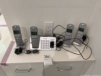 Four Panasonic cordless phones alongside a base station with visible power cords and adapters on a white counter