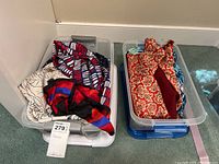 Two clear storage tubs filled with multiple scarves in various colors and patterns including red, blue, black, white, and a red floral design.