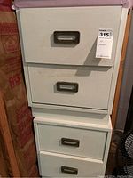 Overview photo showing the two small white dressers stacked with visible wear, scratches, and metal handles on each drawer.